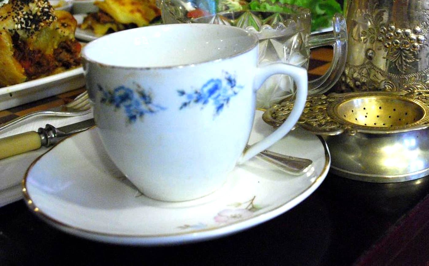 A blue and white china teacup and saucer beside a silver teapot