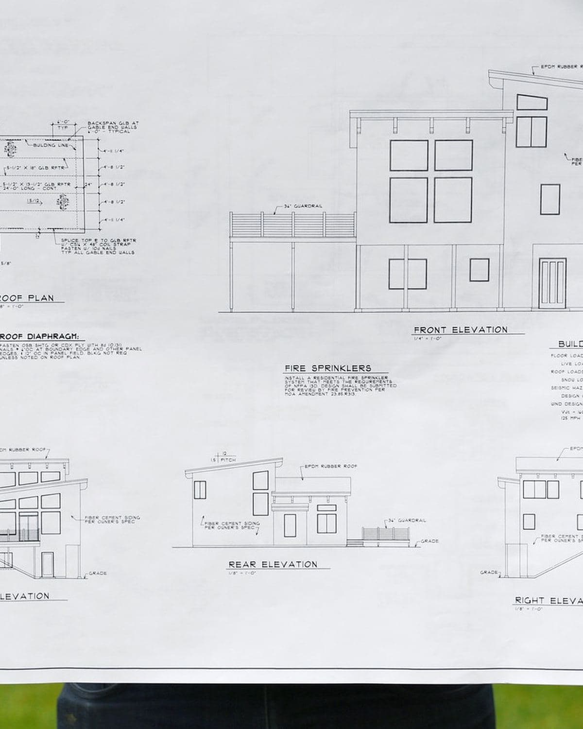 A large sheet of architectural elevation drawings held up to the camera