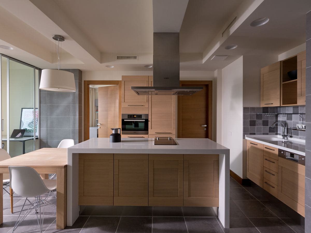 A fitted kitchen with timber cabinets, a white island worktop and a tiled floor