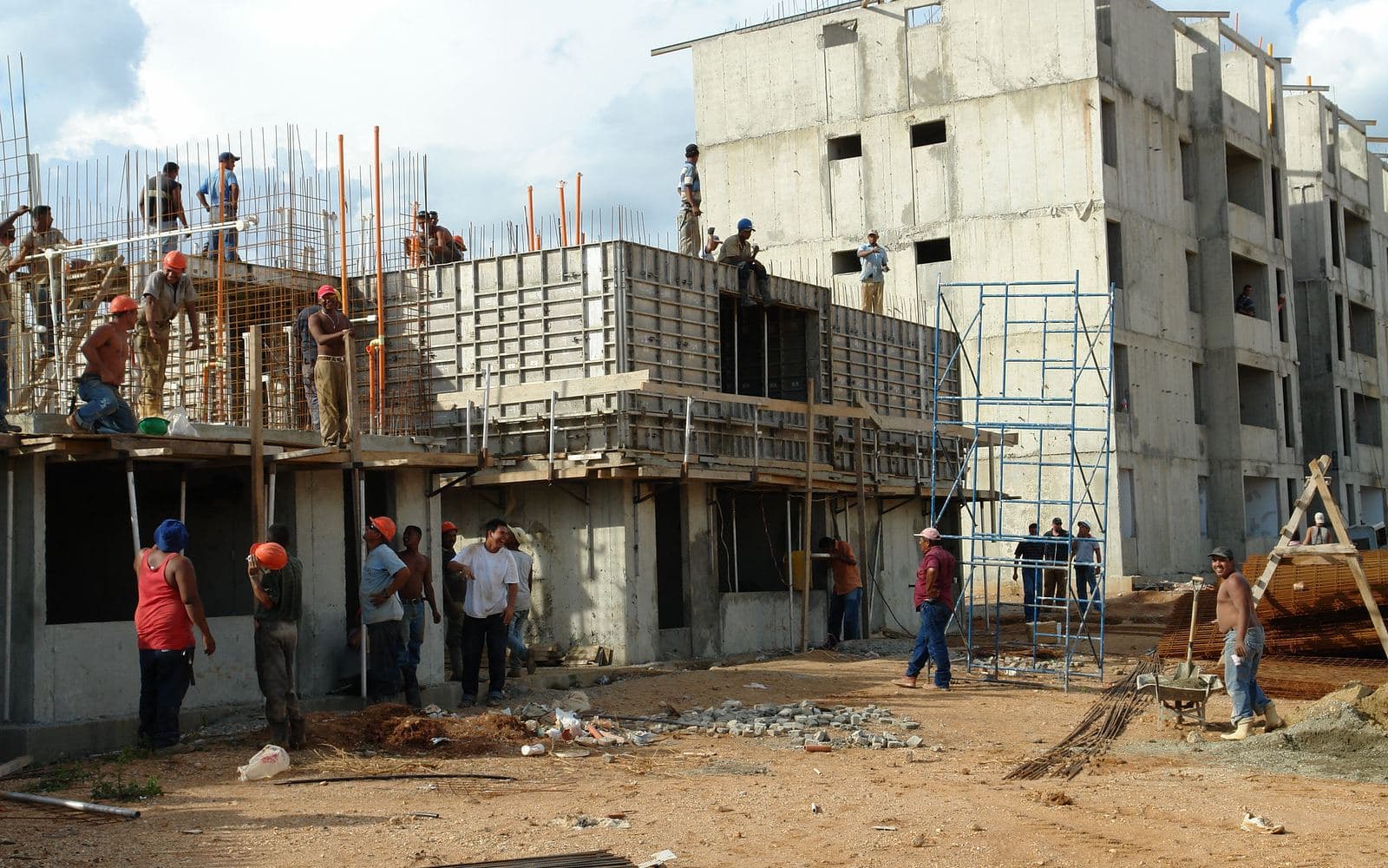 A concrete building going up, with formwork, scaffolding and a crew of workers on a dirt site